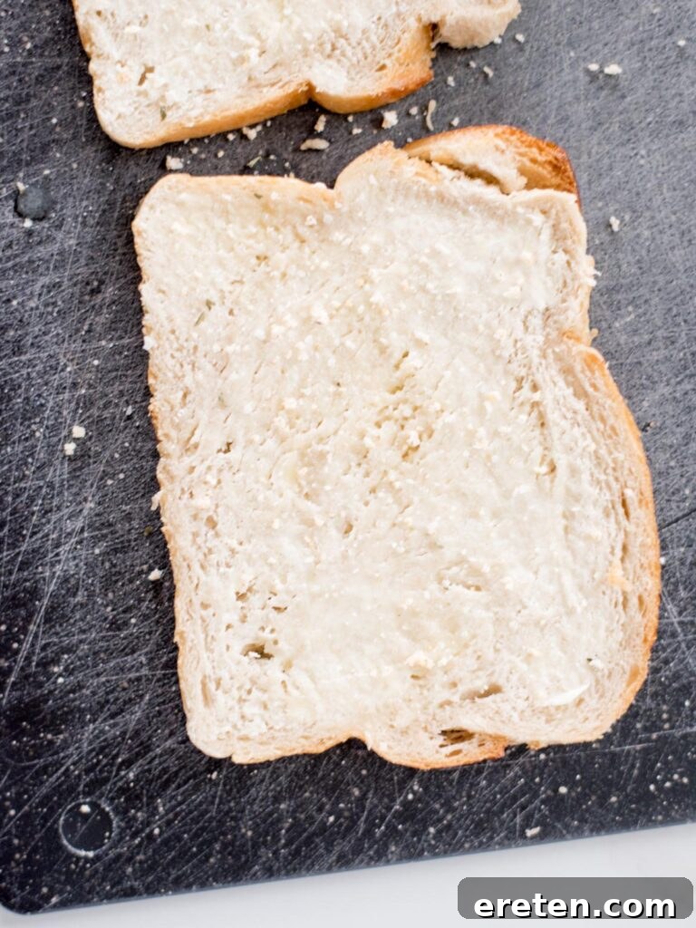 Air Fryer Grilled Cheese Perfection 5 A single slice of buttered bread on a cutting board, generously sprinkled with garlic salt, highlighting the seasoning process.