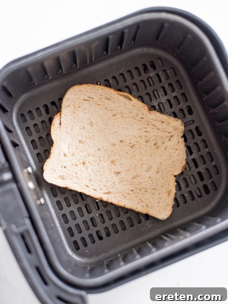 Air Fryer Grilled Cheese Perfection 6 One slice of buttered bread, butter side down, perfectly positioned within the air fryer basket, ready for the cheese layer.