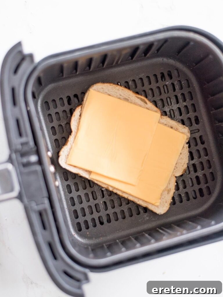 Air Fryer Grilled Cheese Perfection 7 Two slices of American cheese layered on top of the first slice of bread inside the air fryer basket, showing the preparation for melting.