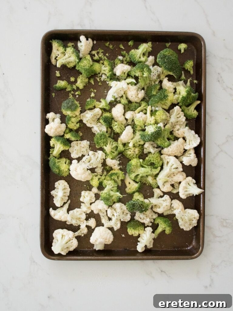 Broccoli and cauliflower on a sheet pan seasoned with salt and pepper, ready for roasting.