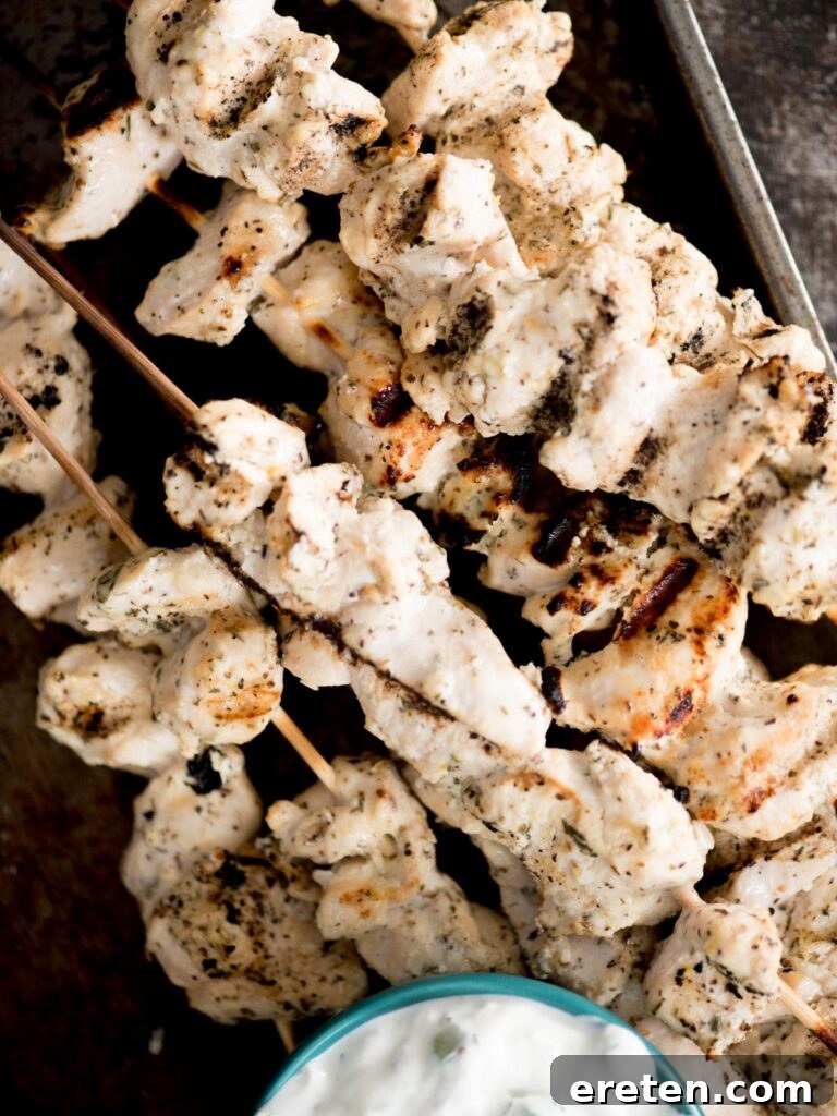 Stacked Greek Grilled Chicken Skewers served with a side of creamy tzatziki sauce, garnished with fresh dill.