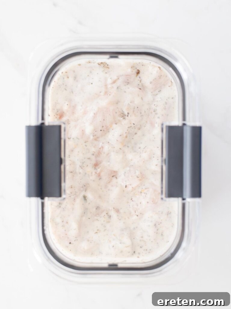 A lid placed on the bowl containing chicken marinating in Greek yogurt sauce.