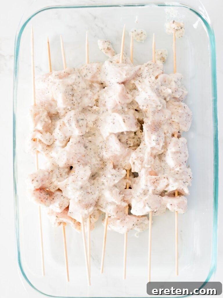 Cubed chicken pieces coated in Greek marinade, neatly threaded onto skewers, ready for grilling.