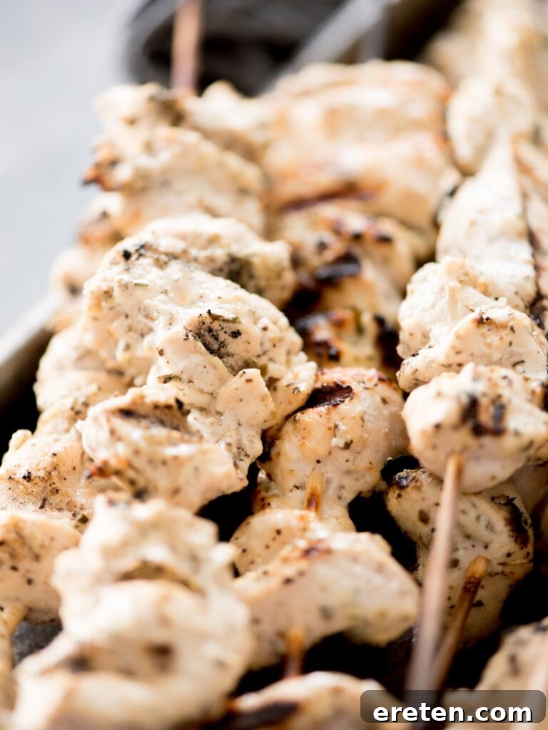 Close-up of freshly grilled Greek chicken skewers, perfectly charred and juicy, served with tzatziki sauce.