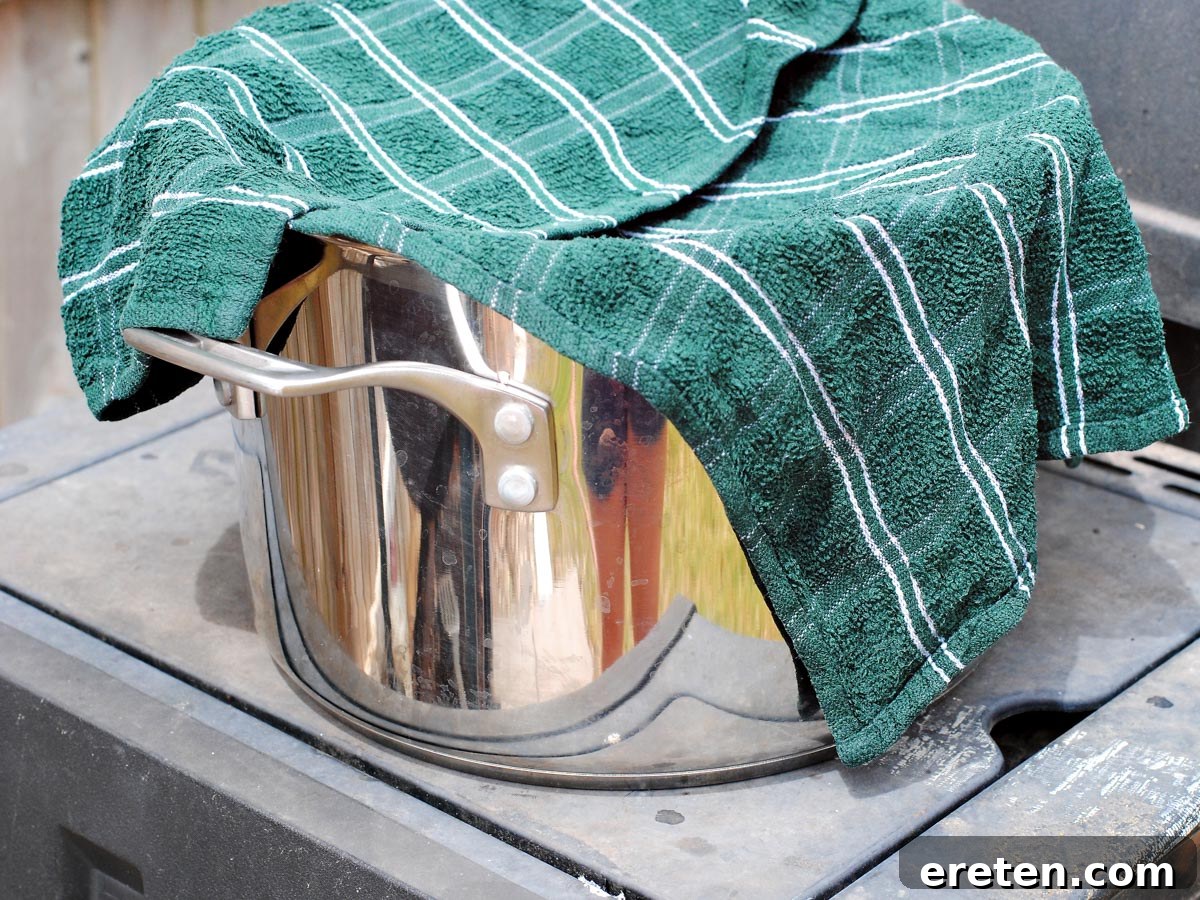 A silver pot with a damp green dish towel draped over it, ready for roasted chiles