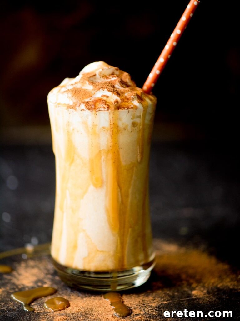 A tall glass filled with a creamy pumpkin milkshake, topped with whipped cream and a generous caramel drizzle, hinting at the perfect autumn treat.
