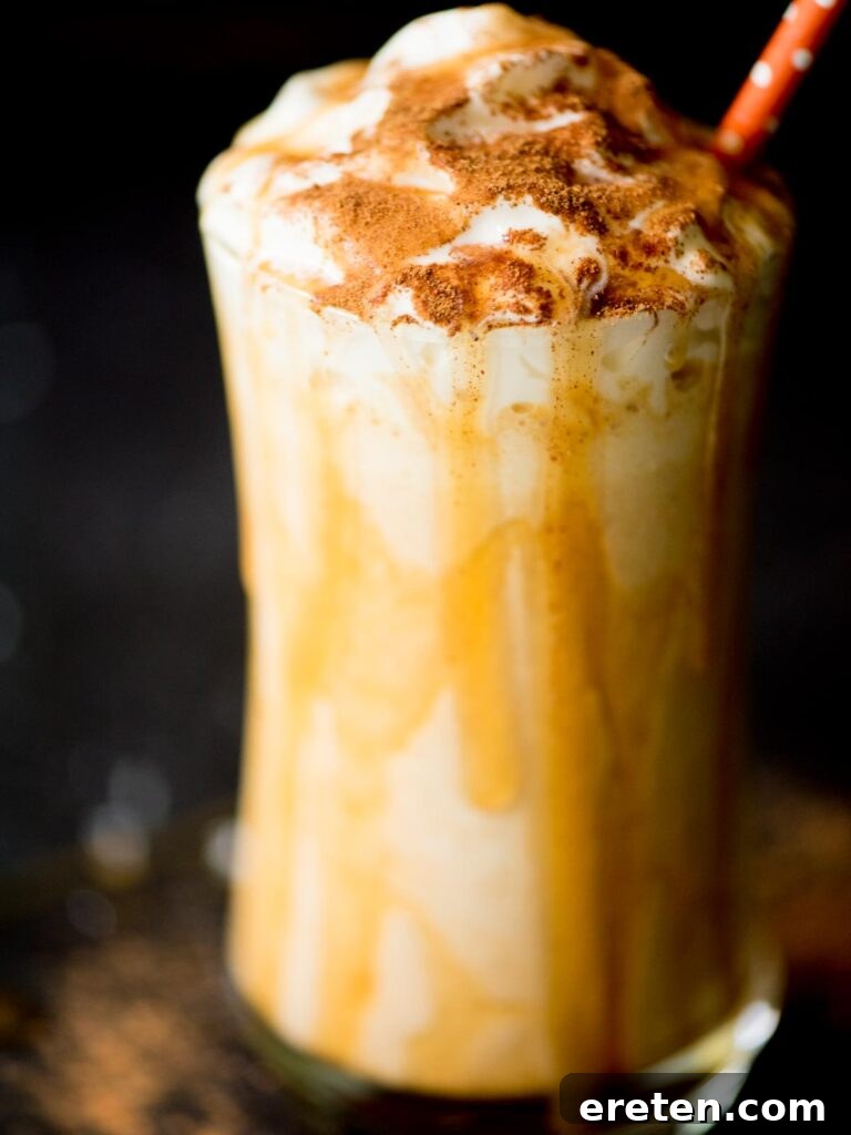 A vibrant pumpkin milkshake in a clear glass, richly topped with whipped cream and a decadent caramel drizzle, set against a warm, inviting backdrop.