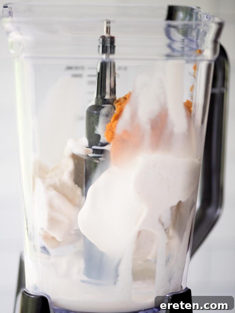 Smooth, orange pumpkin puree being added to the blender with other milkshake ingredients, bringing in the distinct fall flavor.