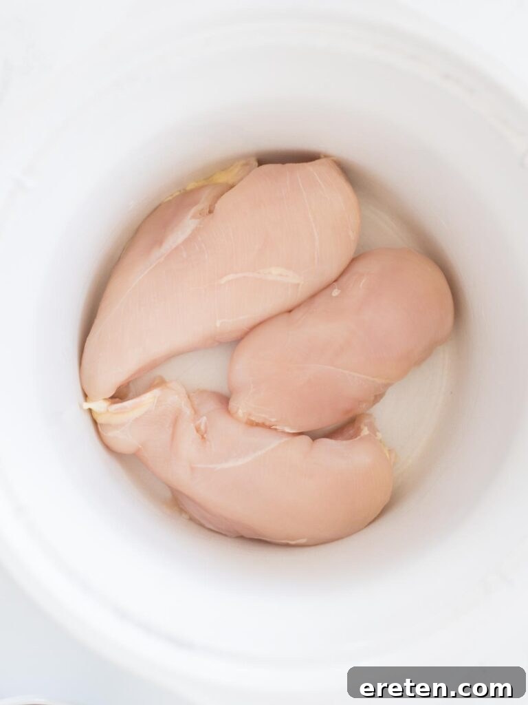 Easy Slow Cooker Mexican Chicken 4 Raw chicken breasts in the bottom of a slow cooker.