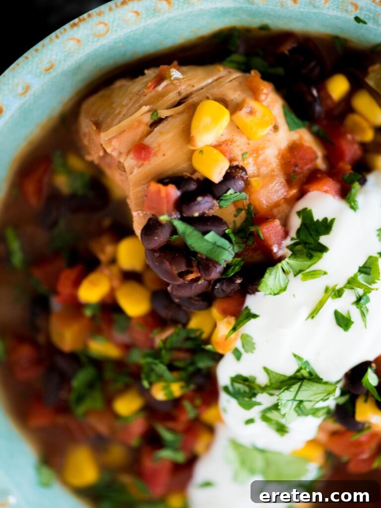 Easy Slow Cooker Mexican Chicken 10 Close-up of slow cooker Mexican chicken in a white bowl, garnished with fresh cilantro and a dollop of sour cream, ready to enjoy.