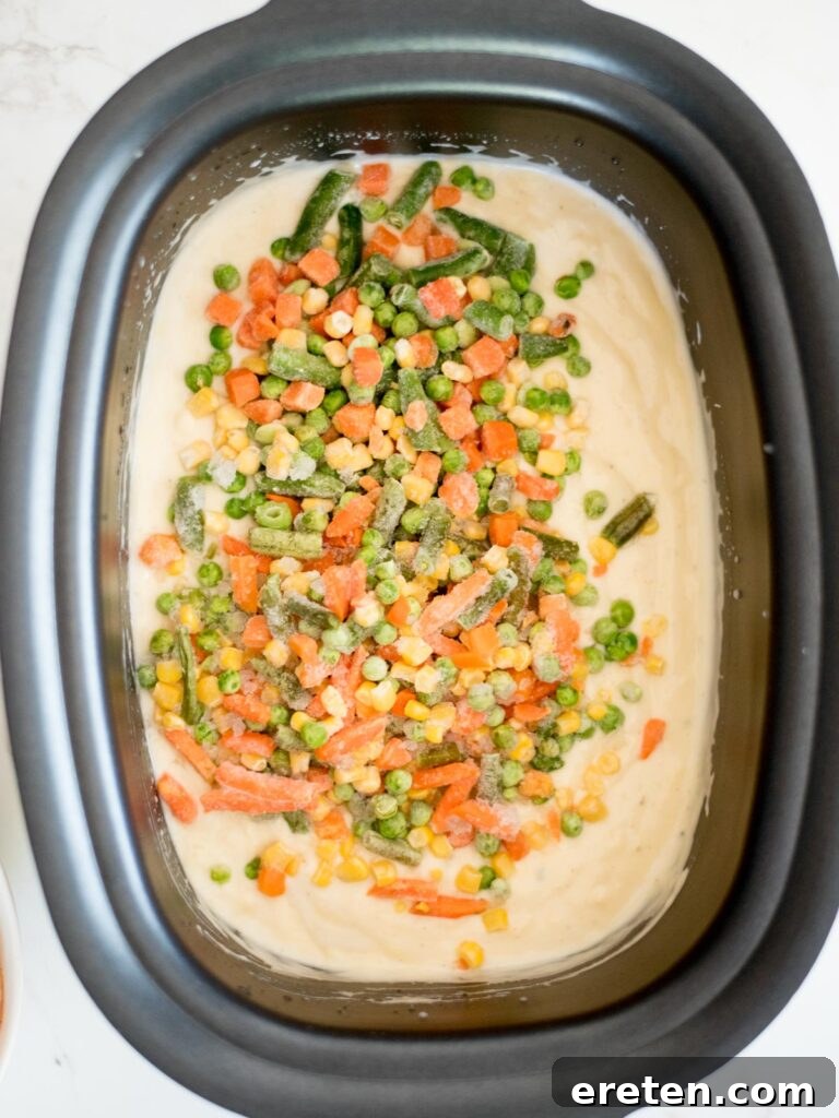 Frozen mixed vegetables freshly added to the creamy sauce mixture in the crockpot.