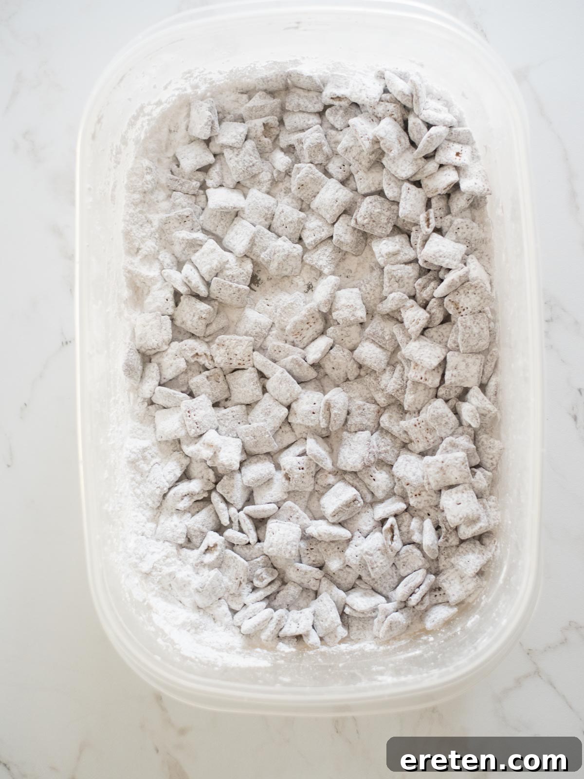 Festive Homemade Muddy Buddies 7 Reindeer Chow perfectly coated in a generous layer of powdered sugar, nestled in a container, looking like a snowy winter treat.