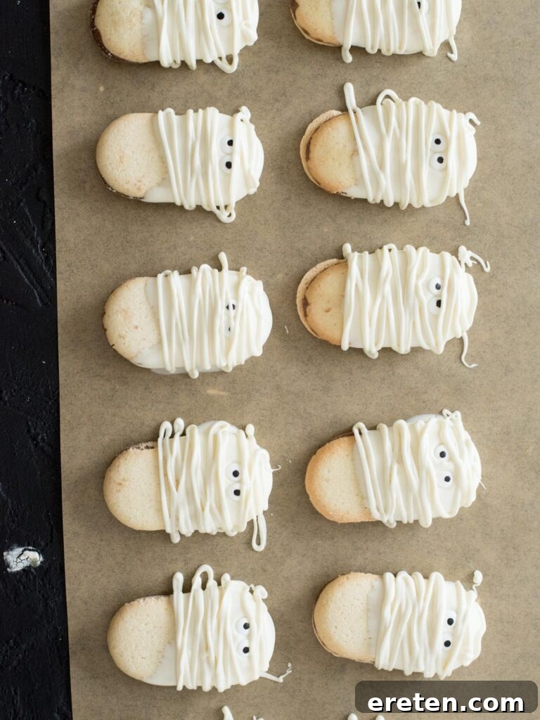 Finished mummy cookies with drizzled almond bark on parchment paper