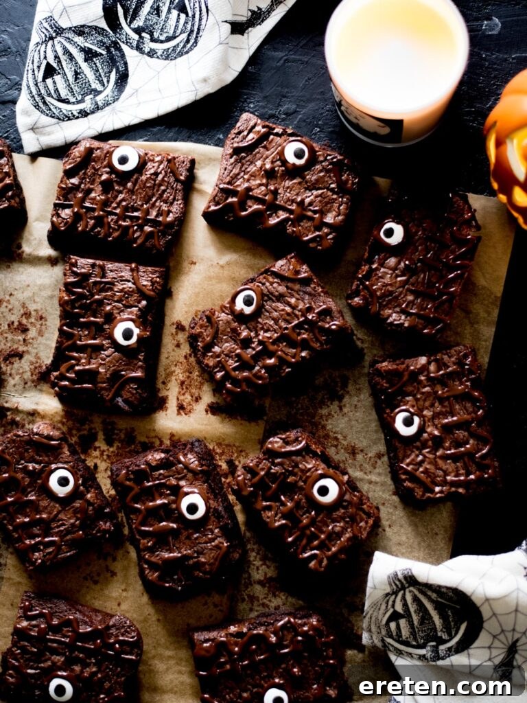 Delicious Halloween brownies adorned with candy eyes, sitting beside a flickering candle, a soft towel, and a decorative pumpkin, setting a perfect spooky scene for a festive treat.