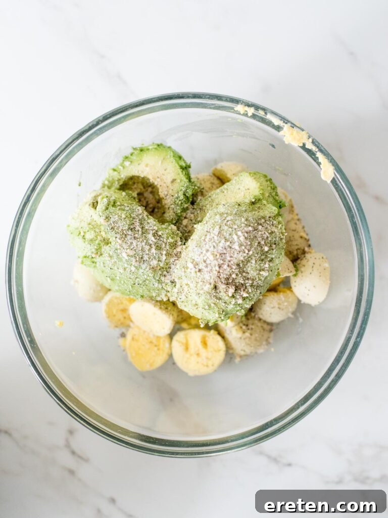 Garlic salt, salt, and pepper sprinkled into the mixing bowl with mashed avocado and egg yolks.