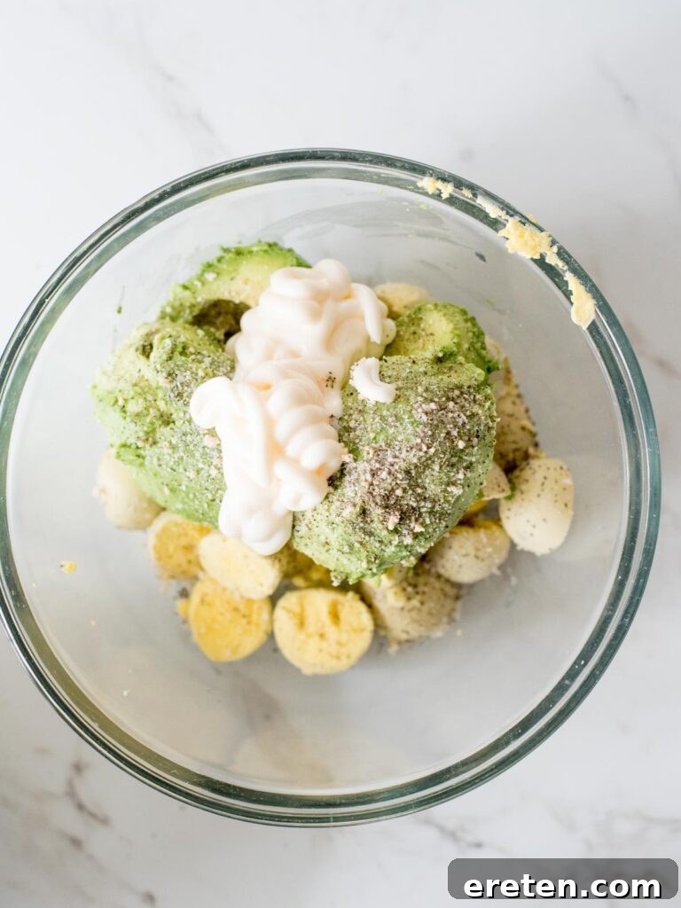 Mayonnaise being stirred into the mixture of seasonings, avocados, and egg yolks in the mixing bowl.