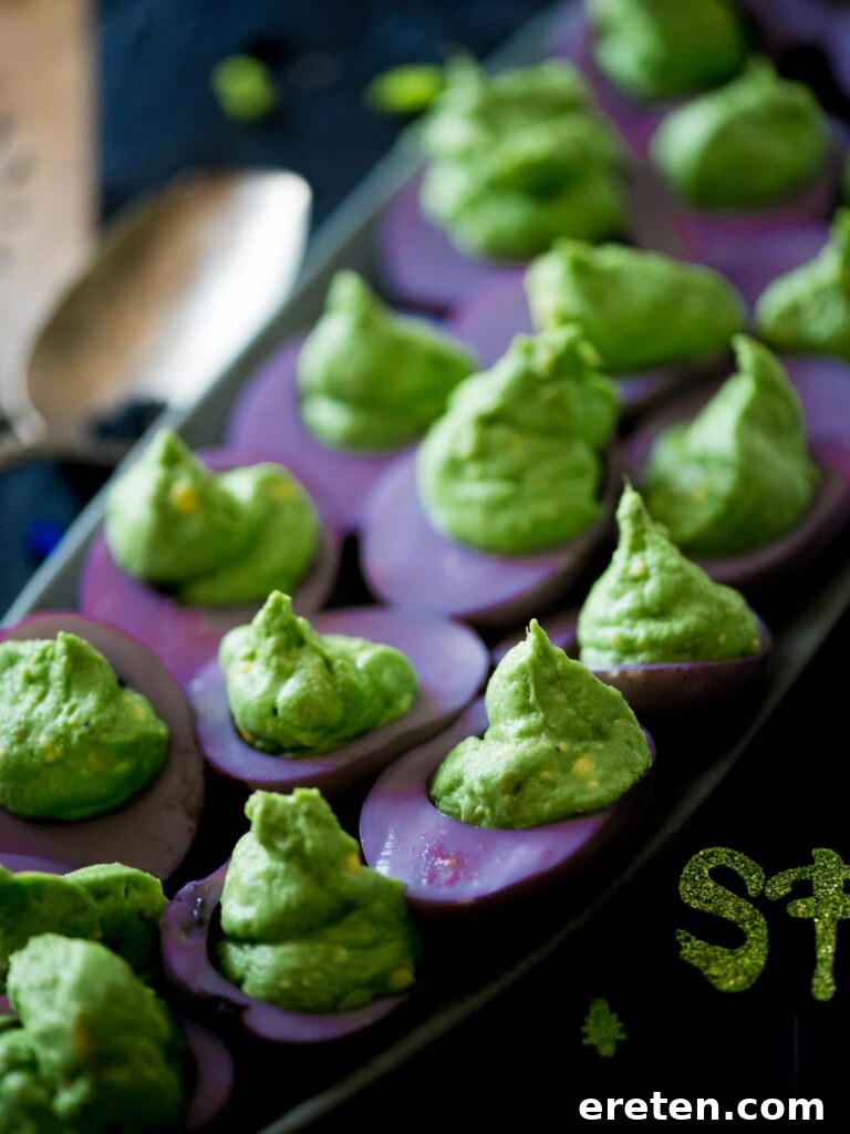 A festive platter showcasing vibrant green and purple Halloween deviled eggs, ready for serving at a party.