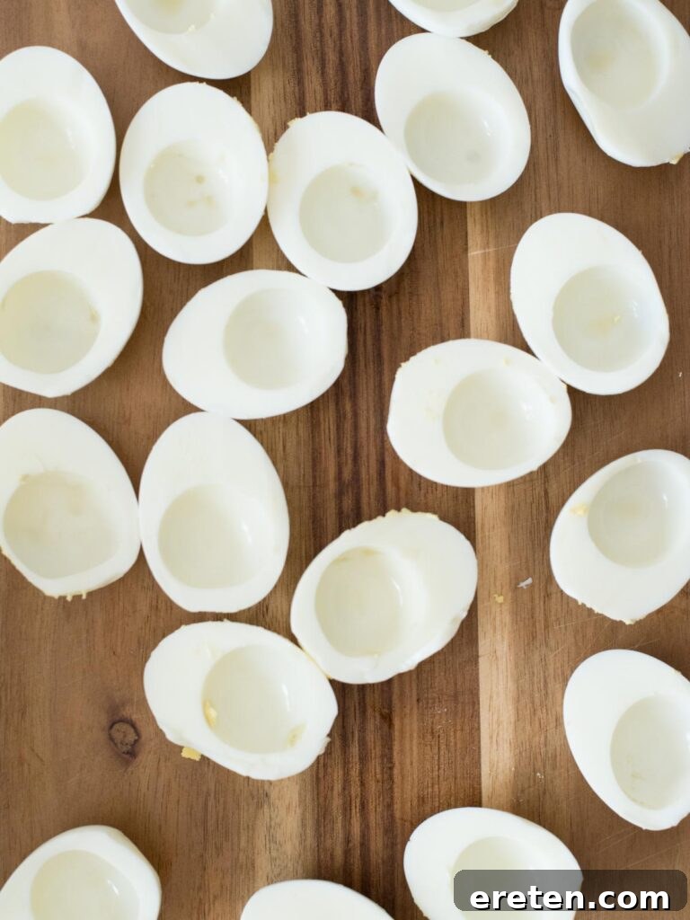 Halved hard-boiled egg whites separated from yolks on a cutting board, ready for coloring.