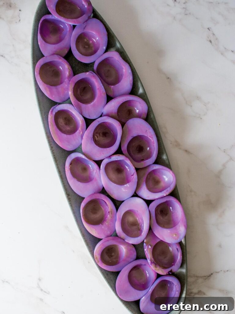Vibrantly colored purple hard-boiled egg whites neatly arranged on a platter, waiting for filling.