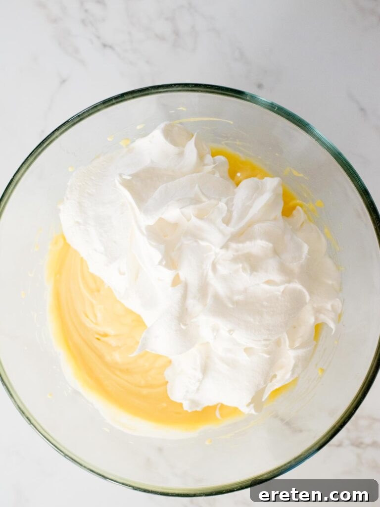 Cool Whip being carefully folded into the smooth pudding filling in a large mixing bowl.