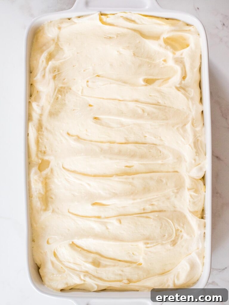 A freshly assembled banana pudding in a casserole dish, with smooth pudding covering bananas and wafers, before the final topping of crushed wafers.