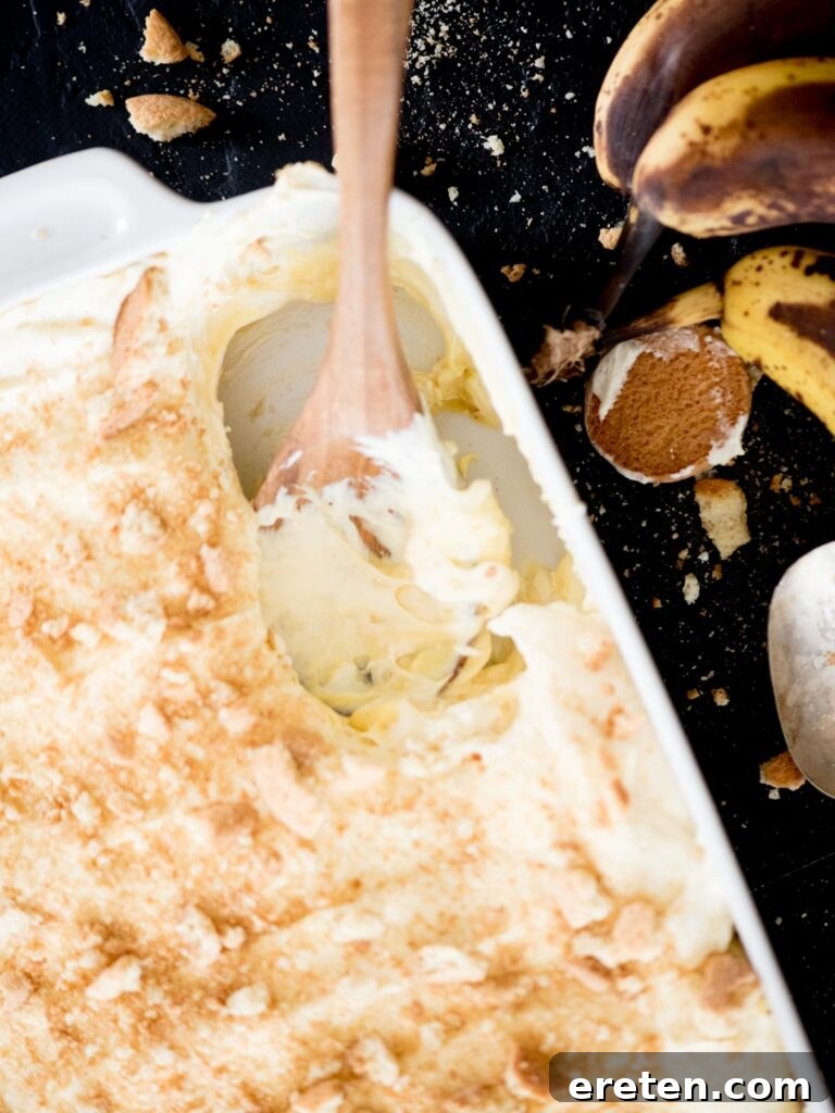 A serving of homemade banana pudding being scooped from a large casserole dish, showing the creamy layers and vanilla wafers.