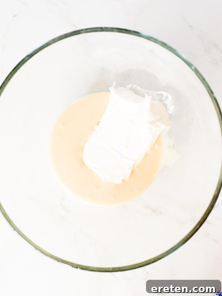 Softened cream cheese combined with sweetened condensed milk in a mixing bowl, being blended.