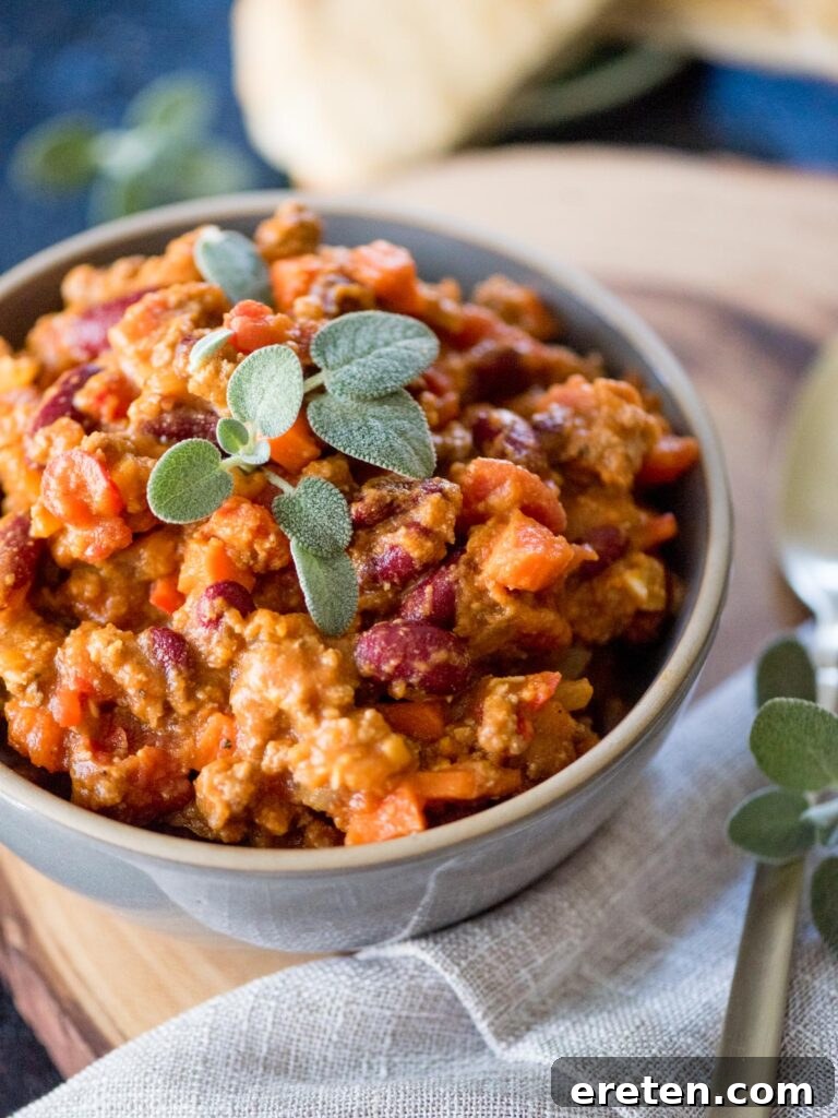 Rich pumpkin chili in a rustic bowl, garnished with fresh sage leaves, ready to be enjoyed as a hearty fall meal.