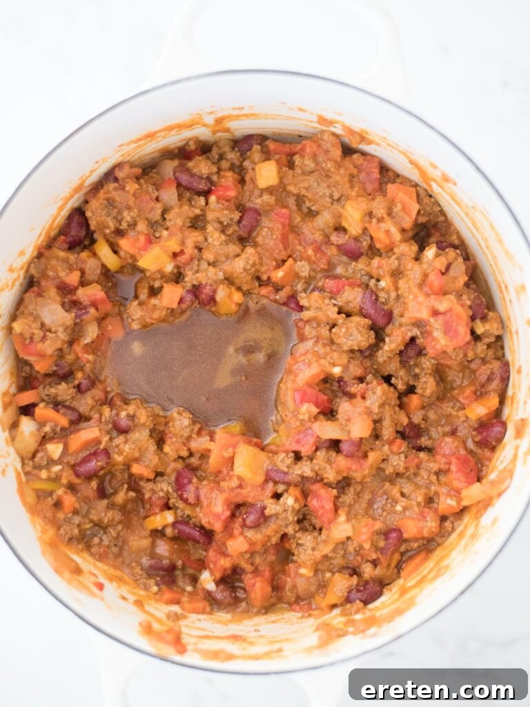 Rich beef broth poured into the pot, simmering with the pumpkin chili ingredients, ready to deepen the flavors.