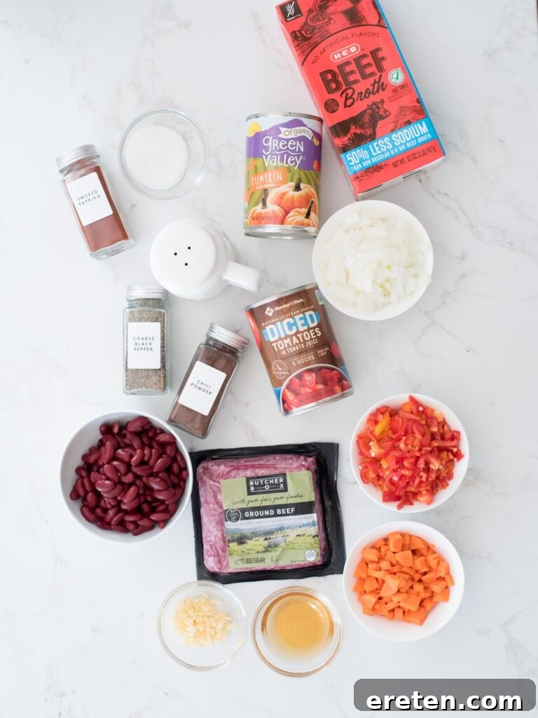 Arrangement of fresh and canned ingredients for pumpkin chili including ground beef, bell peppers, pumpkin puree, and spices.