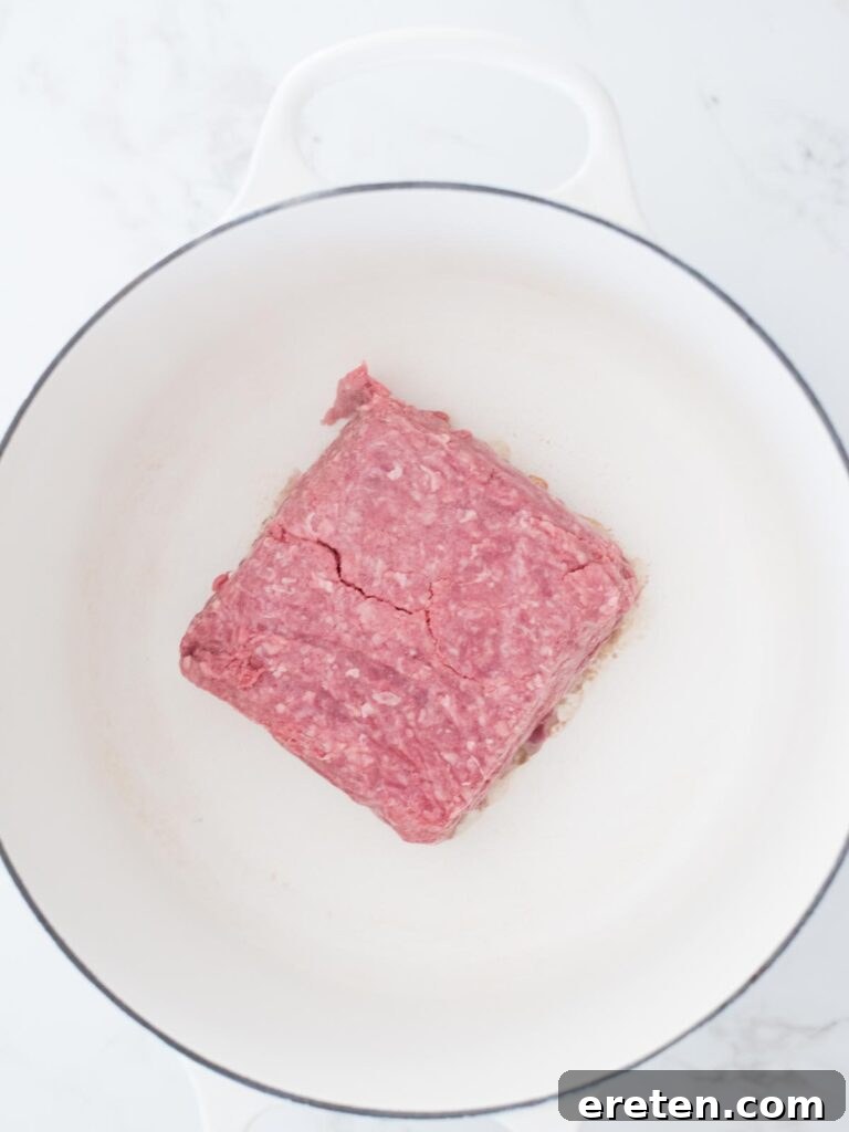 Ground beef browning in a vibrant enamel cast iron Dutch oven, forming the hearty base of the chili.