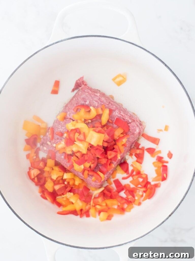 Chopped bell peppers, a mix of vibrant colors, added to the sizzling ground beef in the Dutch oven.