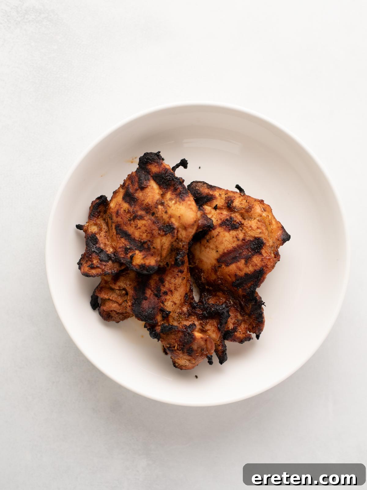 Zesty Street Chicken Tacos 6 A white bowl containing several pieces of grilled, charred chicken with visible grill marks, set against a light background.
