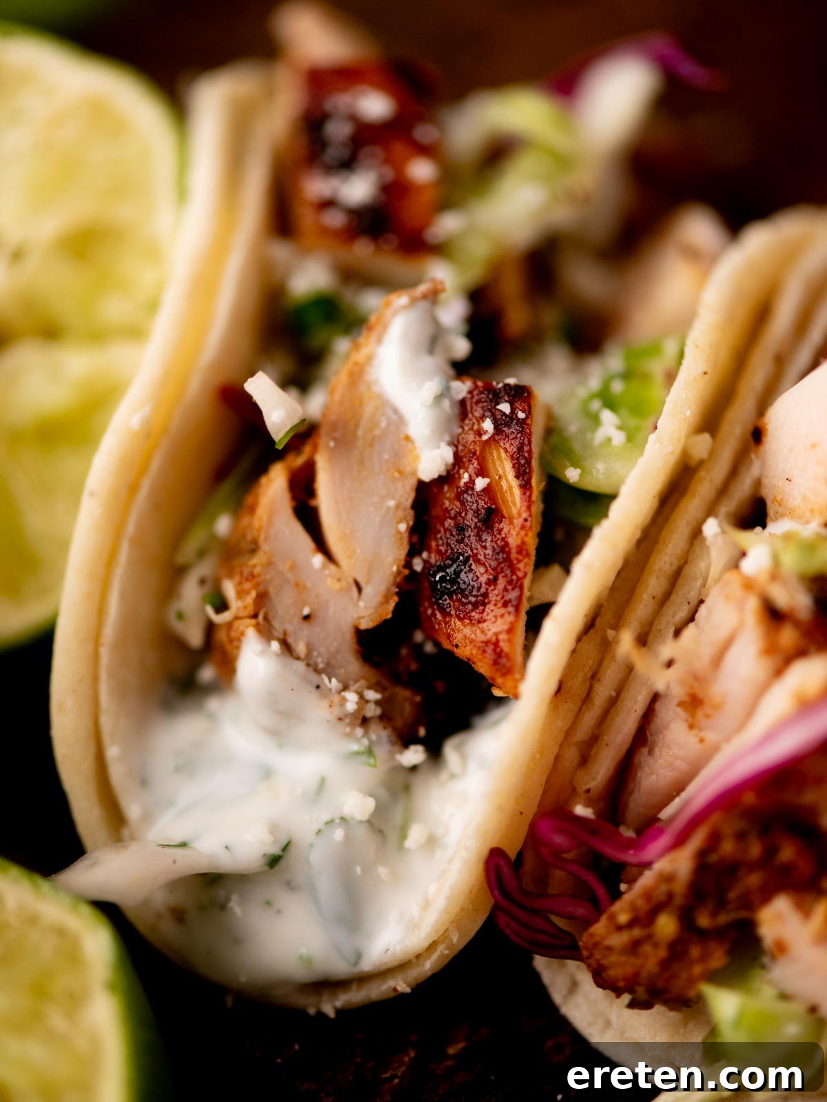 Zesty Street Chicken Tacos 7 Close-up of a chicken taco in a soft tortilla, topped with creamy white sauce, shredded lettuce, and grilled chicken pieces. Lime wedges are visible in the background.