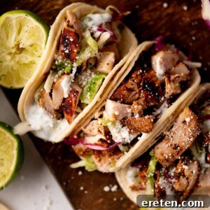 Zesty Street Chicken Tacos 8 Three soft tacos filled with grilled chicken, shredded lettuce, cabbage, cheese, and creamy sauce are arranged on a wooden board with halved limes beside them.