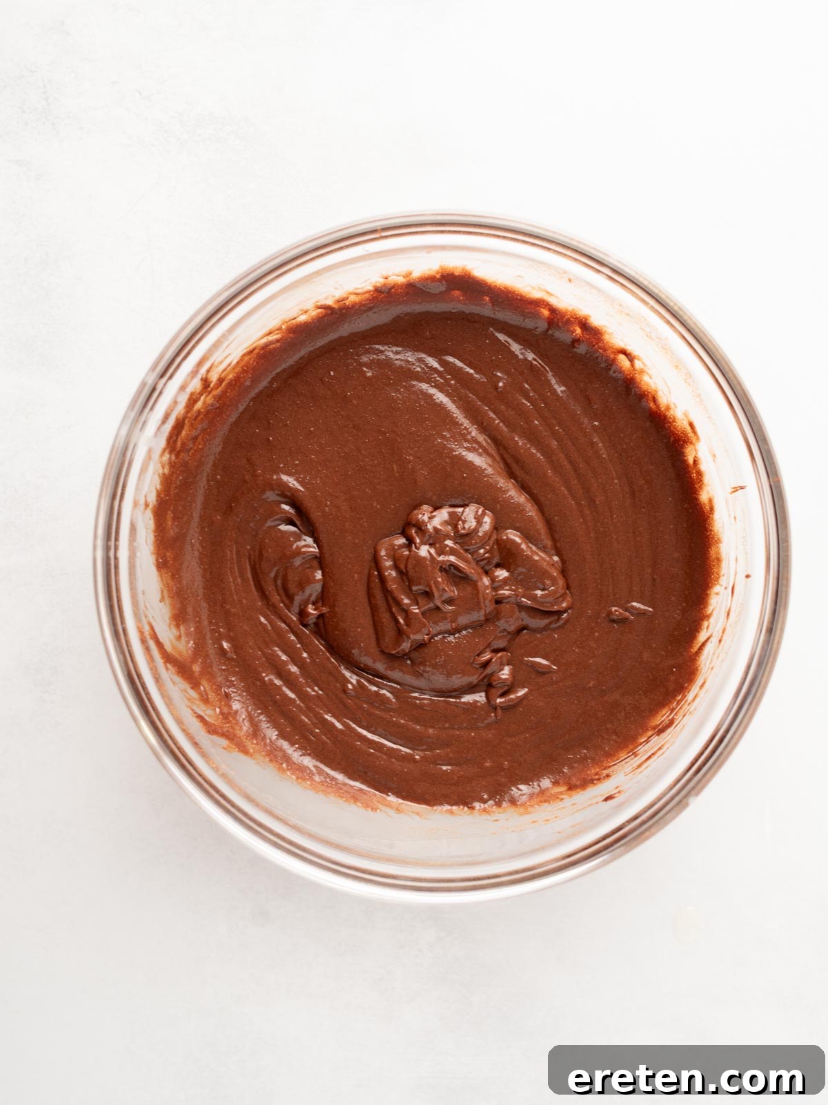 A glass bowl filled with smooth, rich chocolate batter on a white surface, showing the creamy texture after all wet ingredients are combined.