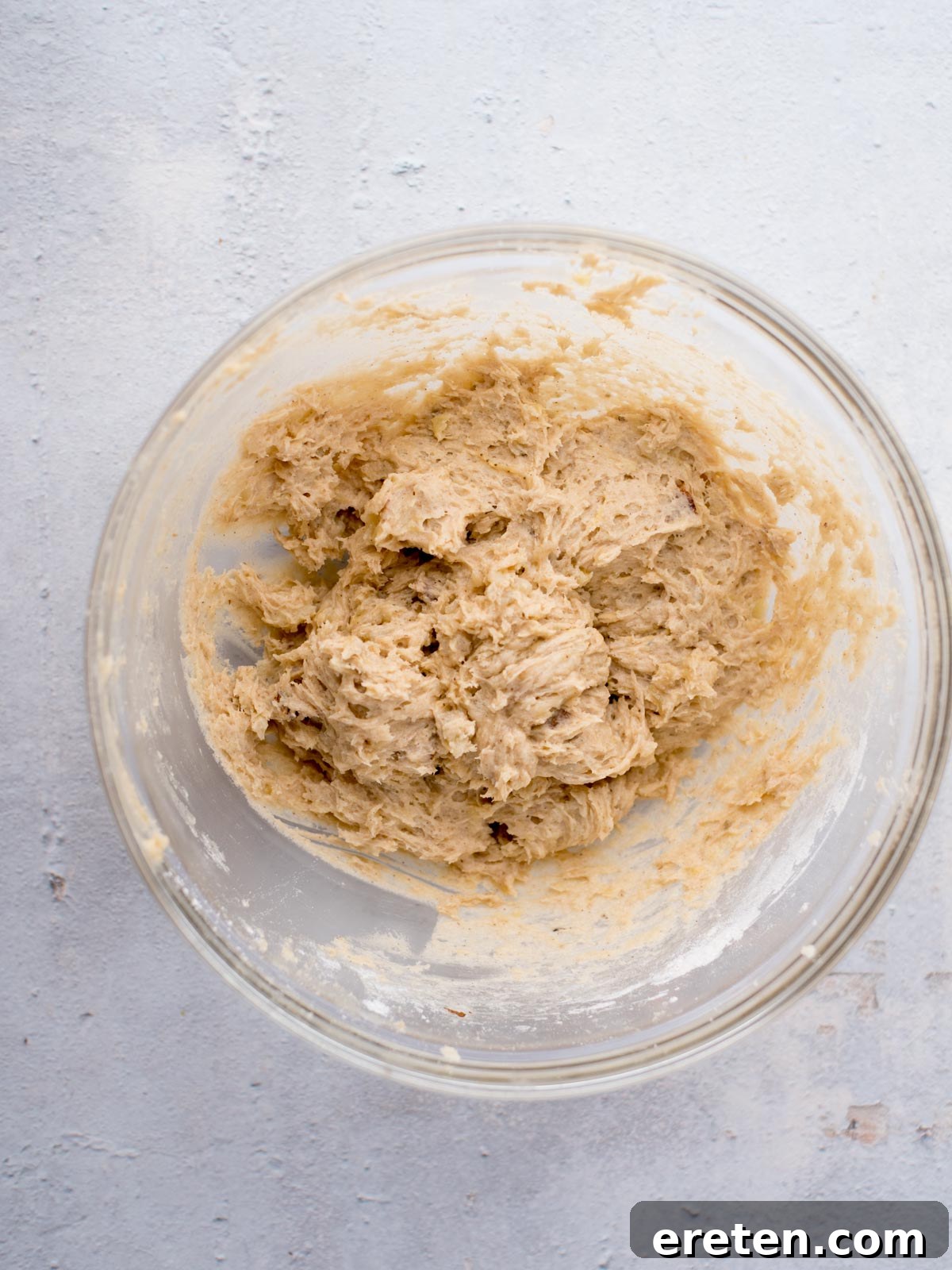 A large glass bowl containing the creamy, pale yellow banana muffin batter after being mixed. The texture is thick and slightly lumpy, ready for the nuts to be folded in.