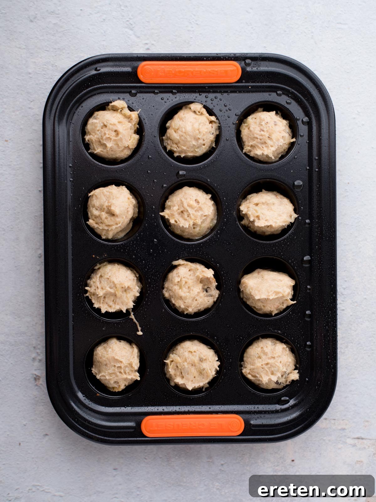 A black mini muffin tin filled with unbaked batter, portioned evenly into each of the twelve cups, ready to go into the oven.