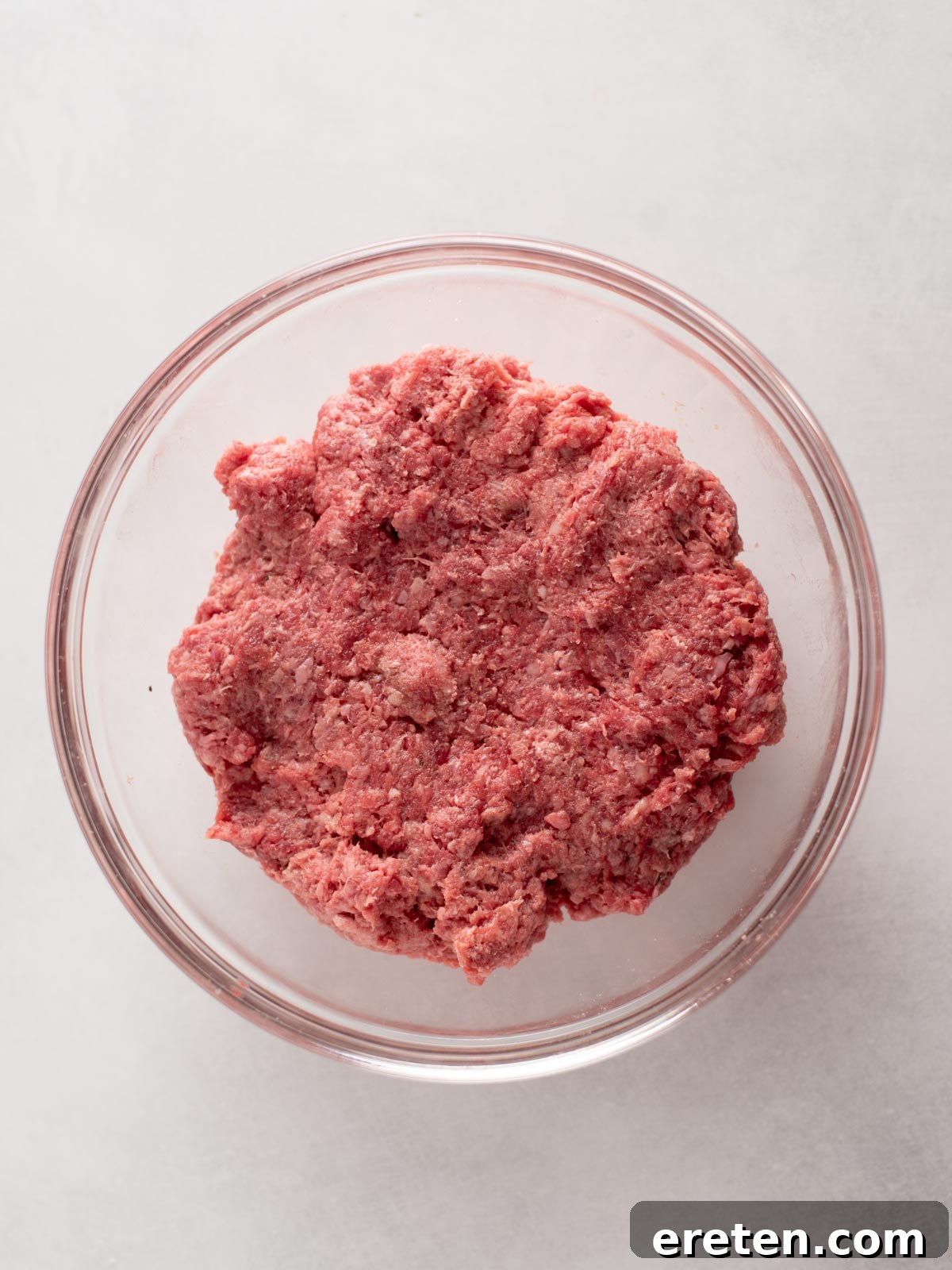 Juicy Grilled Burger Recipe: Charred, Flavor-Packed Patties 4 A clear glass bowl filled with raw ground beef sits on a white surface.