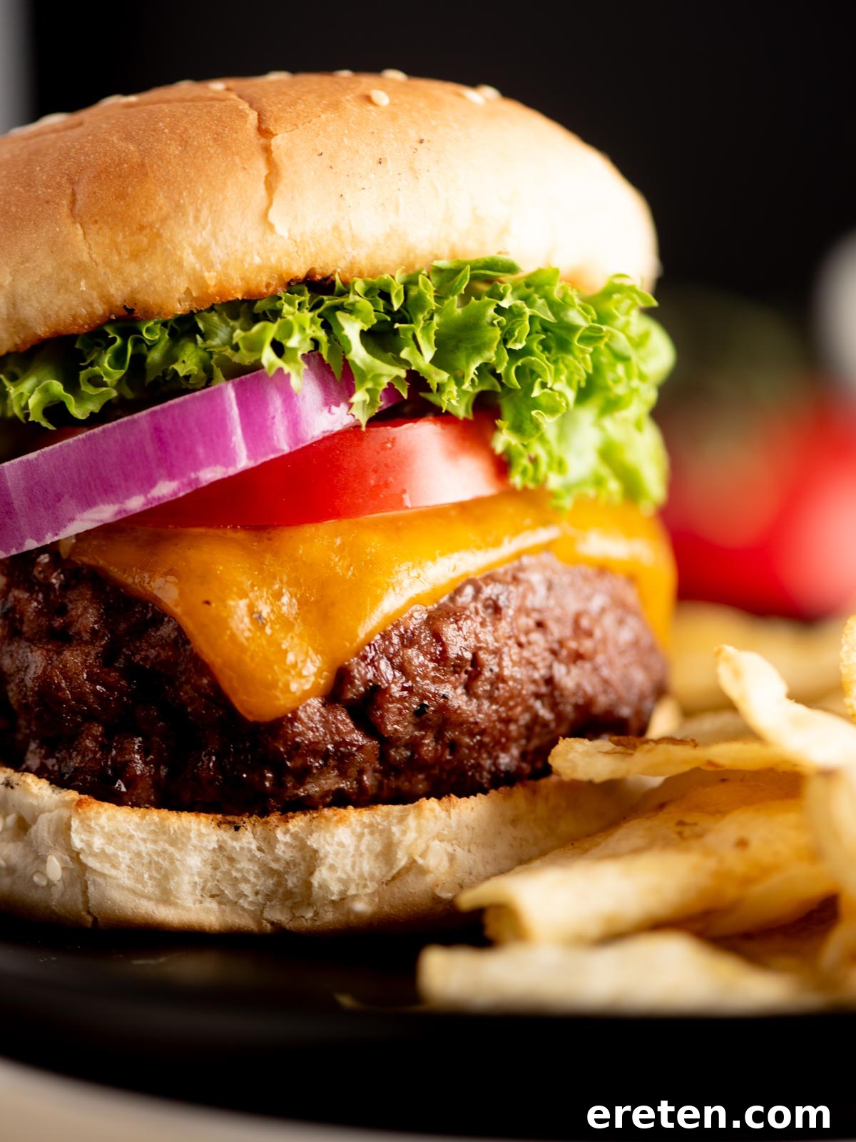 Juicy Grilled Burger Recipe: Charred, Flavor-Packed Patties 5 A close-up of a cheeseburger with lettuce, tomato, red onion, cheddar cheese, and a beef patty on a sesame bun, served with a side of French fries.